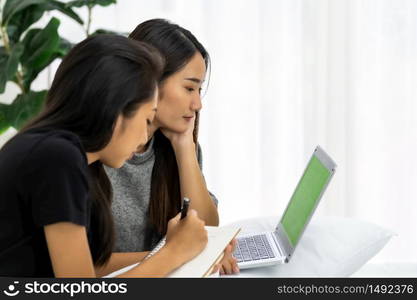 Two Asian university woman using laptop book at home in bedroom for studying while School shutdown due to city lockdown from COVID-19 Pandemic. Education online and study at home concept.