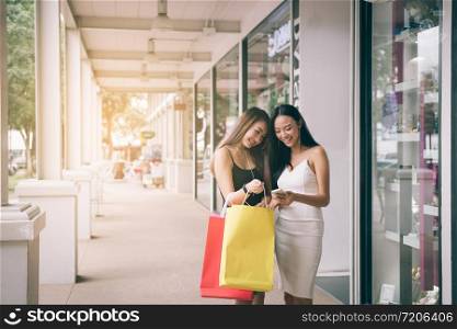 Two asian woman standing at store front with happy watching smart phone at shopping mall center.