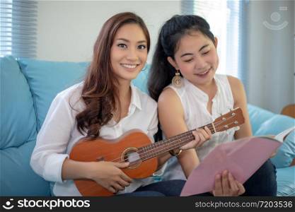 Two asian women are having fun playing ukulele and smiling at home for relax time