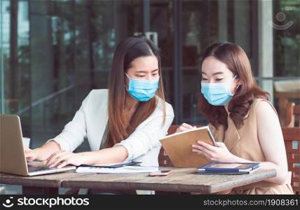 Two asian women are wearing mask to protect virus and using laptop for working together