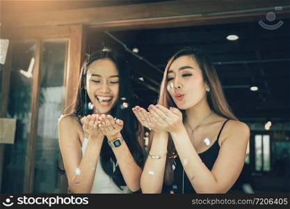 Two asian women blowing paper confetti for a celebration in his home.