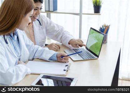 Two asian women doctors discuss meeting doctor&rsquo;s office medical clinic using laptop consulting patient disease. Asian medical lab young women talking together discussing healthcare assistance teamwork