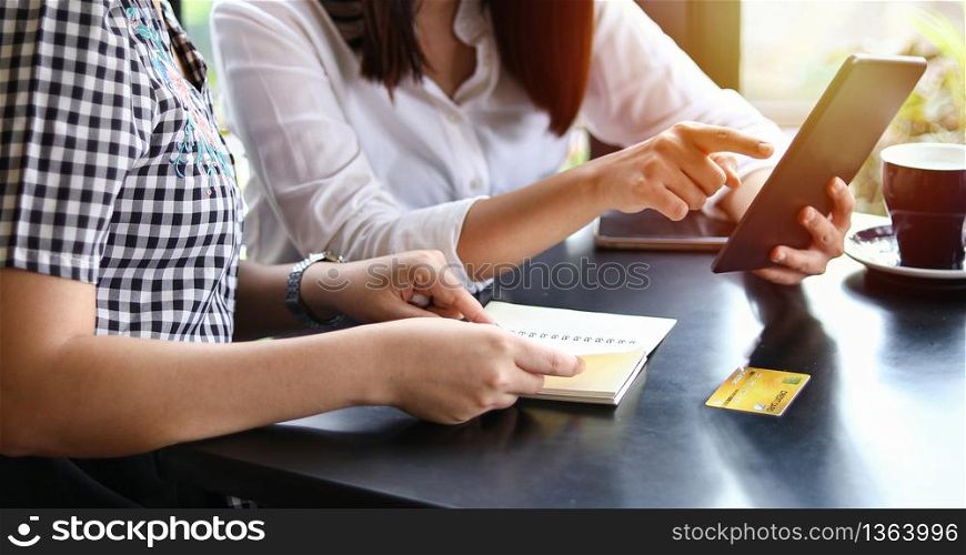 Two Asian women drinking coffee in a cafe and shopping online on smart phones