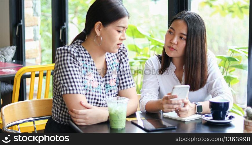 Two Asian women drinking coffee in a cafe and shopping online on smart phones
