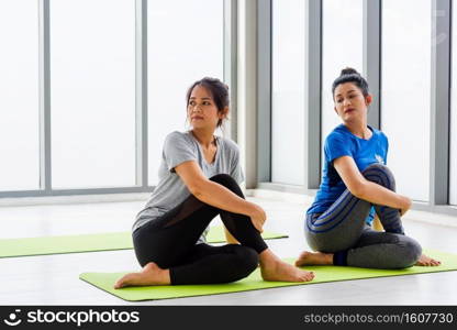 Two Asian women sporty attractive people practicing yoga lesson together, working out at the fitness GYM, Young and senior female exercising do yoga in yoga classes, sport healthy lifestyle