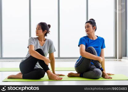 Two Asian women sporty attractive people practicing yoga lesson together, working out at the fitness GYM, Young and senior female exercising do yoga in yoga classes, sport healthy lifestyle