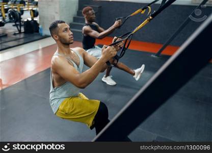 Two athletes in sportswear at exercise machine on training in gym. Fit workout in sport club, healthy lifestyle, fitness. Two athletes at exercise machine, training in gym