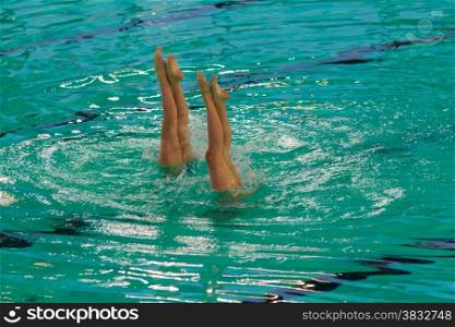 two athletes synchronized swimming during a competion running an upside remaining in apnoea with the legs and feet out of the water