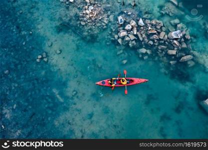 two athletic man floats on a red boat in calm blue waters river. two athletic man floats on a red boat in river
