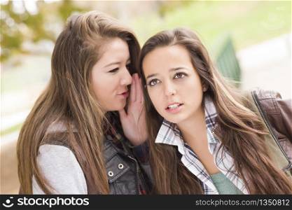 Two Attractive Mixed Race Woman with Backpacks Whispering Secrets Outside.