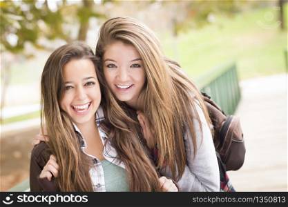 Two Attractive Mixed Race Women with Backpacks Pose for a Portrait Outside.