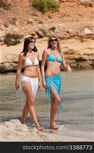 Two attractive woman walking on the beach by the sea