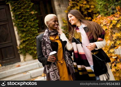 Two attractive young multiethnic women listen music at autumn day