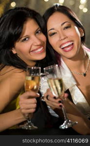 Two attractive young women, one Asian one Hispanic, enjoying champagne in a nightclub