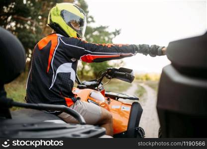 Two atv riders in helmets hits fists for good luck before extreme offroad riding, back view. Freeriding on quad bike, quadbike summer adventure. Two atv riders hits fists for good luck, back view