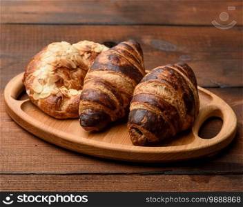 two baked croissants lie on a wooden tray, food on a brown background