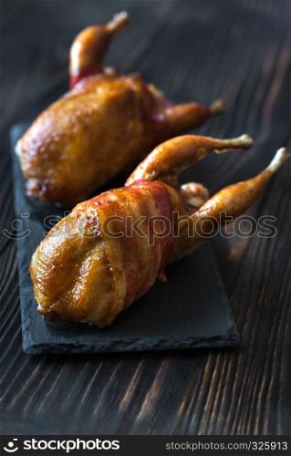 Two baked quails wrapped in bacon on the black stone board