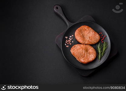 Two baked slices of tuna fillet with spices and herbs on a dark concrete background