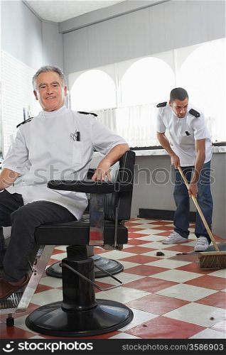 Two barbers in barber shop one sweeping floor