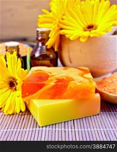 Two bars of homemade soap, bath salt orange, marigold flowers, a wooden mortar, two bottles of oil on the background of a bamboo napkin
