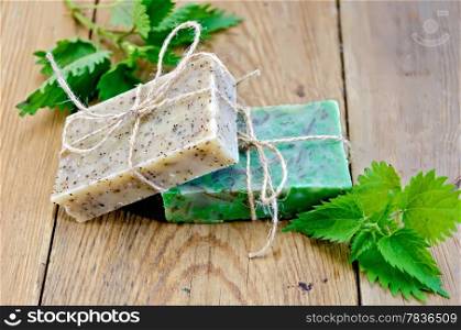 Two bars of homemade soap, tied with twine, nettle on the background of wooden boards