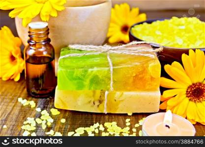 Two bars of homemade soap, yellow bath salt, candle, oil in a bottle and marigold flowers on a background of wooden planks