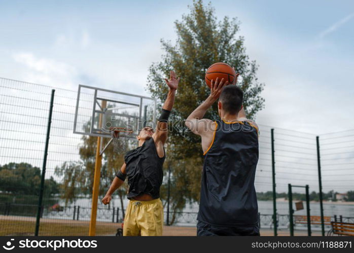 Two basketball player play the game on outdoor court. Male athletes in sportswear on streetball training in park