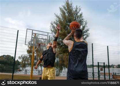 Two basketball player play the game on outdoor court. Male athletes in sportswear on streetball training in park
