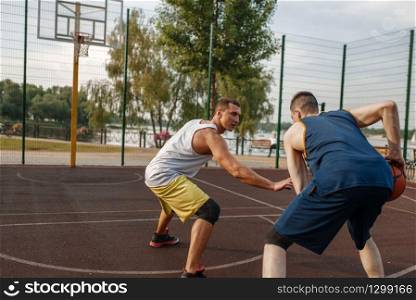Two basketball players playing intense match on outdoor court. Male athletes in sportswear play the game on streetball training. Basketball players playing intense match outdoor