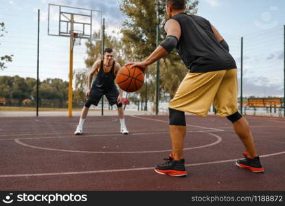 Two basketball players work out tactics on outdoor court. Male athletes in sportswear play the game on streetball training. Two basketball players work out tactics outdoor