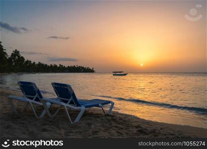 Two beach chairs and boat background on the tropical beach at sunset,Dominican republic,Bahia Principe beach.