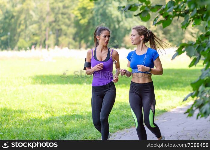 Two beautiful and attractive fitness girls are jogging in the park on a sunny morning