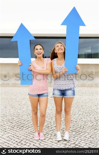 Two beautiful and happy girls holding a giant blue arrow