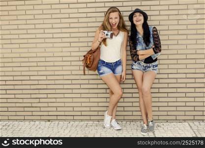 Two beautiful and young girlfriends having fun, in front of a brick wall