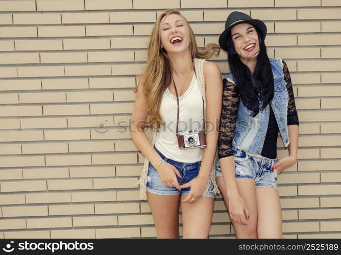 Two beautiful and young girlfriends having fun, in front of a brick wall