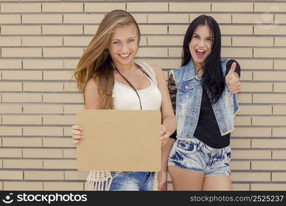 Two beautiful and young girlfriends having fun, in front of a brick wall