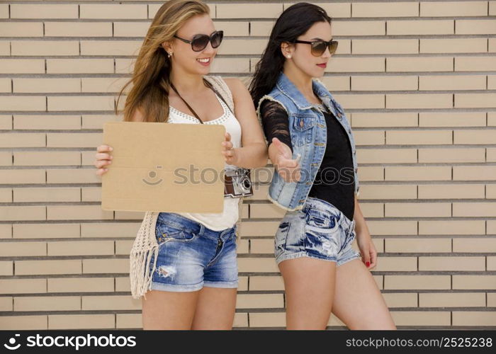 Two beautiful and young girlfriends having fun, in front of a brick wall