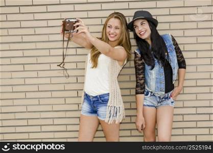 Two beautiful and young girlfriends taking pictures with a vintage camera