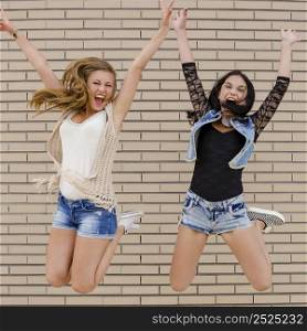 Two beautiful and young jumping in front of a brick wall