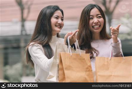 Two beautiful asian women smiling with happy, holding paperbags and doing window shopping. Winter Season, Friendship and Sales Discount Concept.