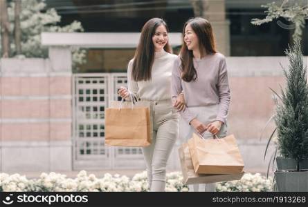 Two beautiful asian women smiling with happy, holding paperbags and doing window shopping. Winter Season, Friendship and Sales Discount Concept.