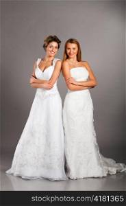 two beautiful brides are standing in wedding dress on grey background