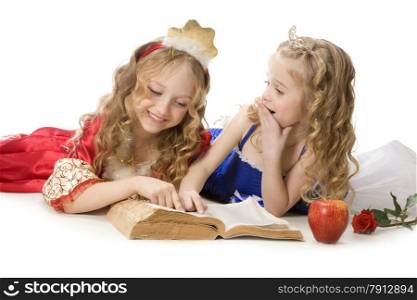 Two beautiful emotional little girls with long blonde hair in the princess costumes reading a magic book at the white background. Red and blue empire dresses