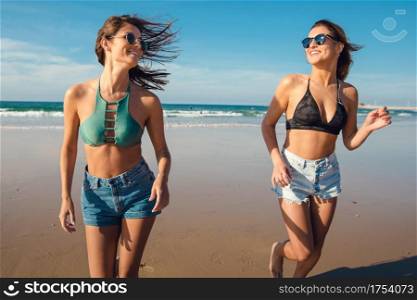 Two beautiful female friends in bikini running at the beach and having fun together