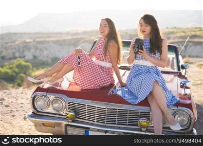 two beautiful girl in a retro dress are photographed on camera  on  mountain landscape in Cappadocia near a red retro car
