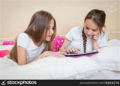 Two beautiful girls in pajamas lying and using digital tablet