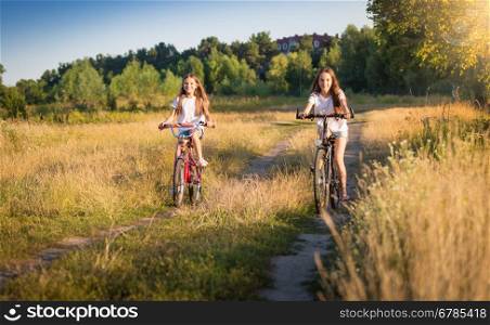 Two beautiful girls riding bicycles on meadow at sunny day