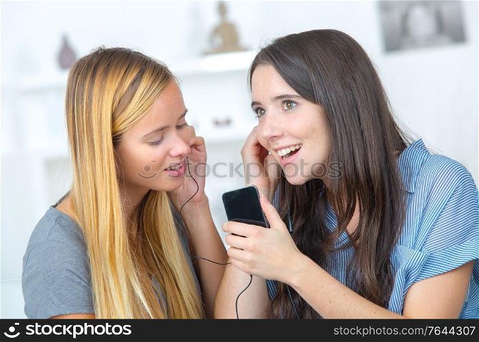 two beautiful girls sharing headphones listening to music