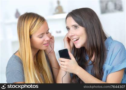 two beautiful girls sharing headphones listening to music