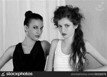 two beautiful girls with amazing hair styles and elegant dress posing indoor near an old fashion door posing with attractive poses looking towards the camera